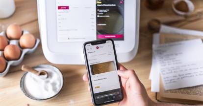 Eine Hand hält ein Smartphone vor dem Monsieur Cuisine