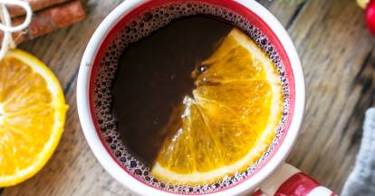 Ein Becher mit Kinderpunsch von oben fotografiert, daneben Tannenzweite und Orangen