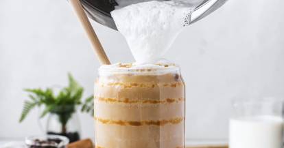 Jemand gießt Milchschaum aus dem Mixbehälter des Monsieur Cuisine auf einen Kaffee