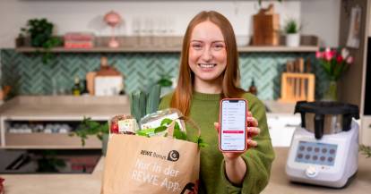 Isy von ZauberMix mit einer TĂŒte voller Lebensmittel von REWE und ihrem Smartphone