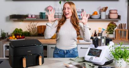 Junge Frau in einer Küche zwischen einem Airfryer und dem Monsieur Cuisine