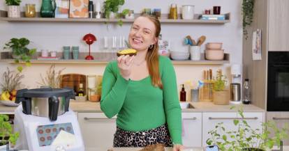 Junge Frau in einer Küche mit Monsieur Cuisine, hält eine Scheibe Brot in der Hand und freut sich