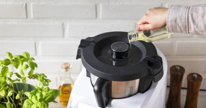 Jemand gießt Öl aus einem Kännchen auf den Deckel des Monsieur Cuisine