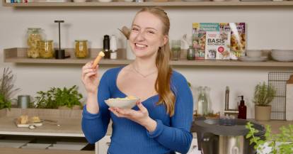 Junge Frau in einer Küche mit einer Schale und einem Snack in der Hand