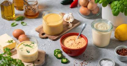 Mehrere soßen in Schalen und Gläsern, daneben Eier, Chilischoten, Zitrone und Gewürze