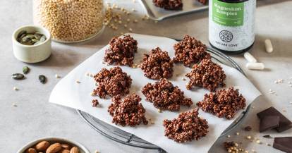 Schokoladen-Crossies auf Butterbrot-Papier, daneben Mandeln und Magnesium-Tabletten