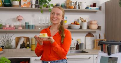 Junge Frau mit einem Stück Kuchen in einer Küche, neben dem Monsieur Cuisine