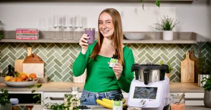 Junge Frau mit einem Blaubeershake in einer Küche neben dem Monsieur Cuisine