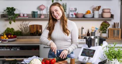 Junge Frau mit langen Haaren schneidet Gemüse, neben ihr steht ein Monsieur Cuisine