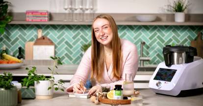 Junge Frau in einer Küche, neben ihr ein Monsieur Cuisine und Produkte von Nature Love