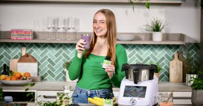 Junge Frau in einer Küche mit einem Monsieur Cuisine. In der Hand Magnesium-Tabletten
