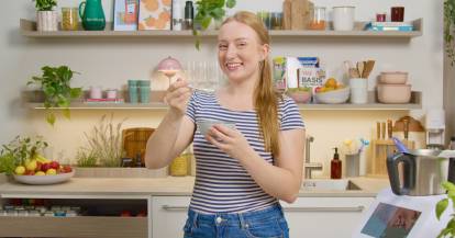 Junge Frau in einer Küche mit einer kleinen Schüssel und einem Löffel in der Hand