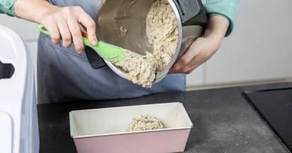 Jemand holt Brotteig mit einem Spatel aus dem Mixbehälter des Monsieur Cuisine