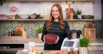 Frau mit langen Haaren in einer Küche mit Monsieur Cuisine, in ihrer Hand eine Plätzchendose