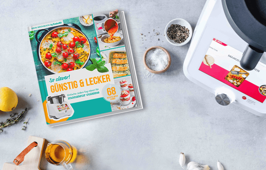 Neues ZauberMix-Kochbuch "Günstig & Lecker" liegen neben dem Monsieur Cuisine und umringt von Zutaten auf einer Arbeitsplatte