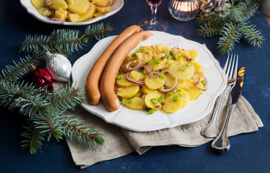Weißer Teller mit Kartoffelsalat und zwei Würstchen in weihnachtlicher Deko