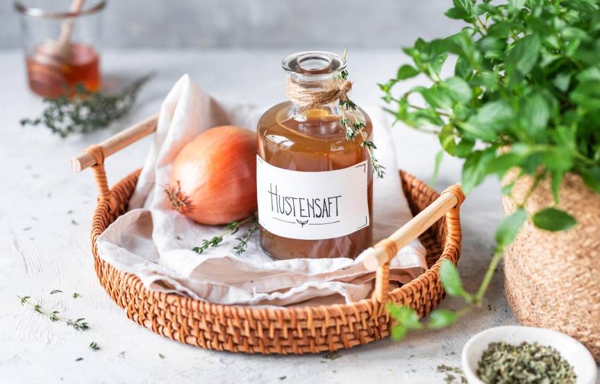Eine Flasche Hustensaft und eine Zwiebel, daneben Kräuter