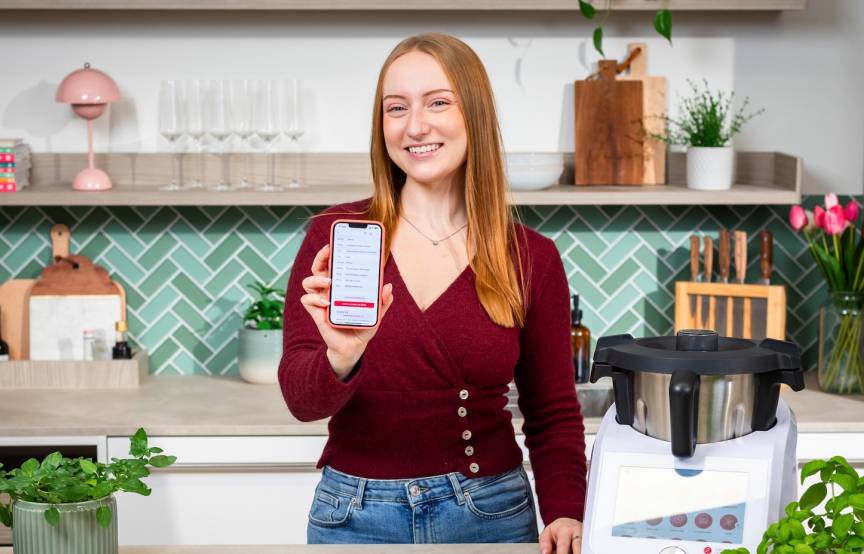 Isy von ZauberMix mit ihrem Telefon und dem Warenkorb von REWE auf dem Bildschirm