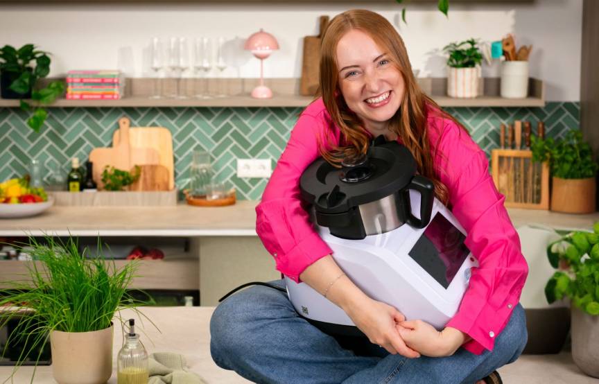 Eine Frau sitzt auf der Arbeitsplatte ihrer Küche und hält den Monsieur Cuisine im Arm