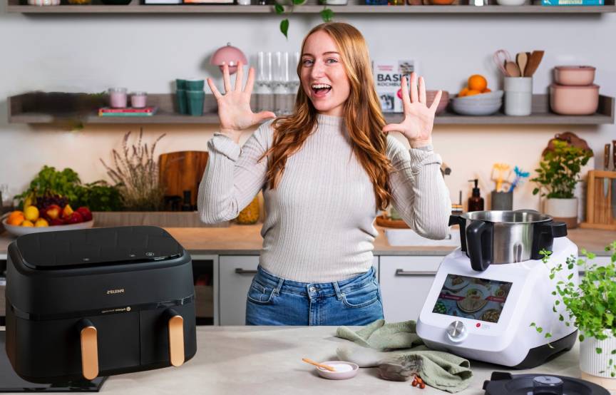 Junge Frau in einer Küche zwischen einem Airfryer und dem Monsieur Cuisine