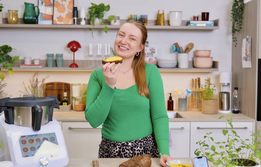 Junge Frau in einer Küche mit Monsieur Cuisine, hält eine Scheibe Brot in der Hand und freut sich
