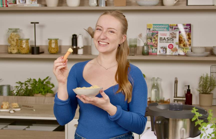 Junge Frau in einer Küche mit einer Schale und einem Snack in der Hand
