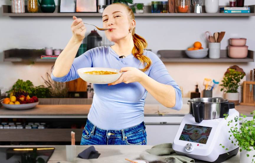 Junge Frau in einer Küche mit einem Teller Tomatensuppe, neben dem Monsieur Cuisine