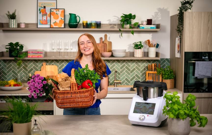 Junge Frau mit einem Korb voll Gemüse in einer Küche, neben dem Thermomix®