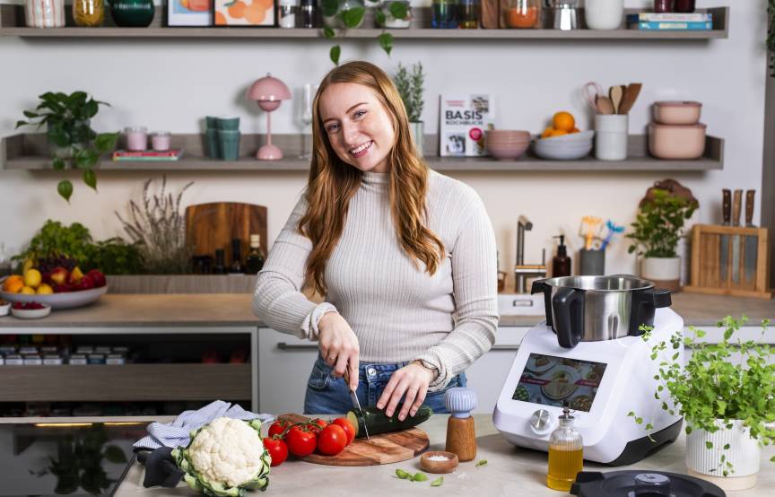 Junge Frau mit langen Haaren schneidet Gemüse, neben ihr steht ein Monsieur Cuisine