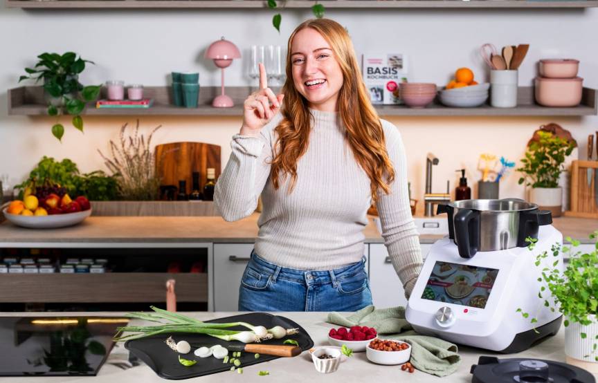 Junge Frau in einer Küche mit dem Monsieur Cuisine und einem Schneidebrett