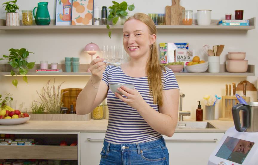 Junge Frau in einer Küche mit einer kleinen Schüssel und einem Löffel in der Hand
