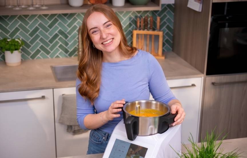 Eine Frau in einer Küche, neben dem Monsieur Cuisine, darin Kürbissuppe