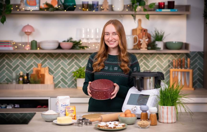 Frau mit langen Haaren in einer Küche mit Monsieur Cuisine, in ihrer Hand eine Plätzchendose