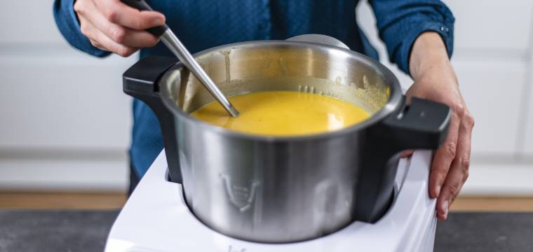 Person, die Suppenkelle in Monsieur Cuisine mit Kürbissuppe hält