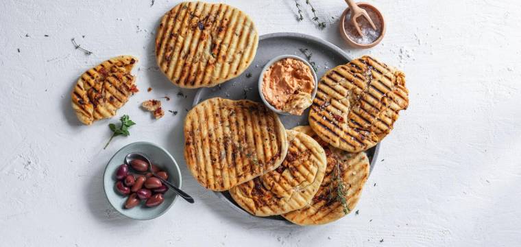 Grillbrot mit Oliven und Dip auf grauem Teller