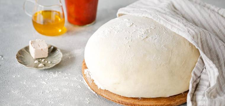 Pizzateig halb abgedeckt mit einem Küchentuch