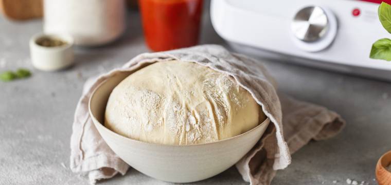Aufgegangener Pizzateig in einer Schüssel, halb abgedeckt mit einem Küchentuch. Aufgegangener Pizzateig in einer Schüssel, halb abgedeckt mit einem Küchentuch.