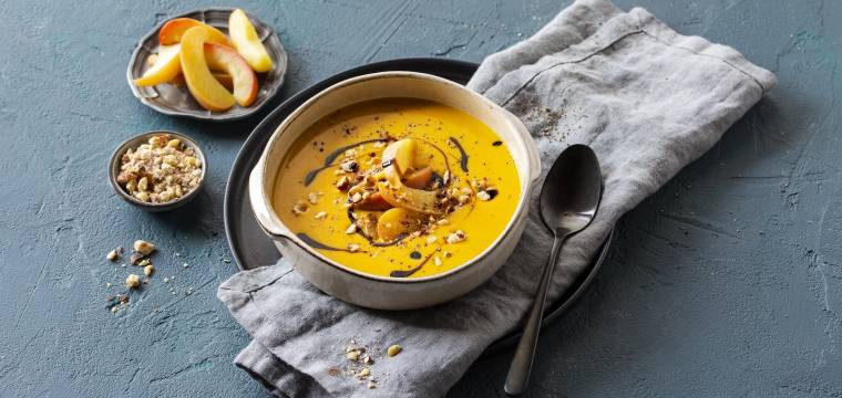 Eine Schüssel mit Kürbissuppe auf einem grauen Tuch vor blaugrauem Hintergrund