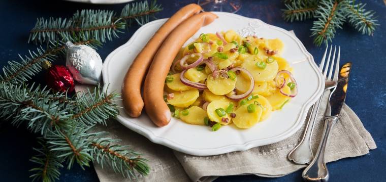 Weißer Teller mit Kartoffelsalat und zwei Würstchen in weihnachtlicher Deko