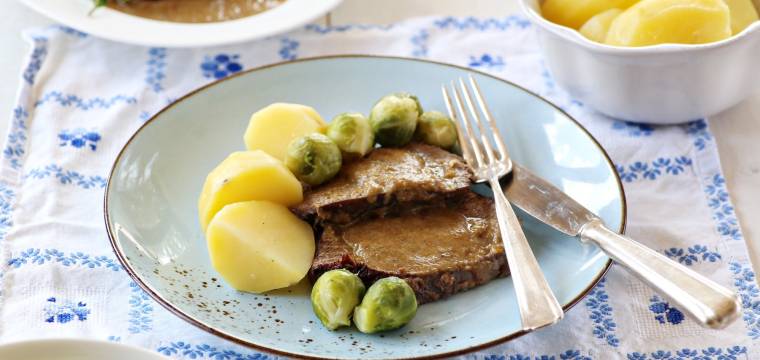 Zwei Scheiben Sauerbraten mit Kartoffeln und Rosenkohl auf hellem Teller