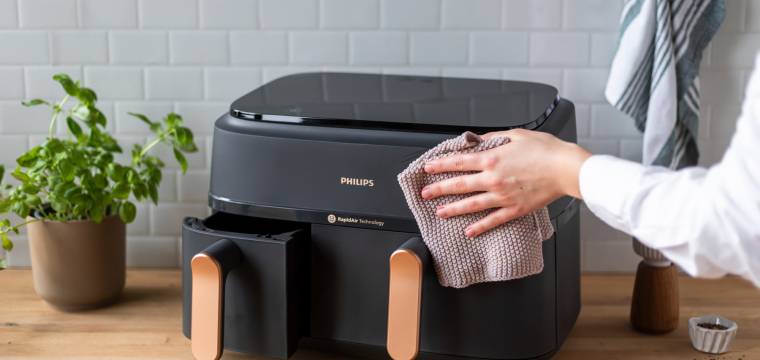Eine Hand hält einen Lappen und wischt die Heißluftfritteuse ab