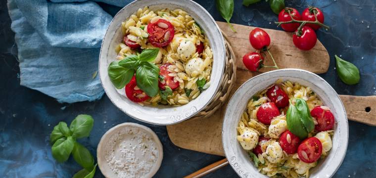 Orzo mit Tomate, Mozzarella, Basilikum in zwei Schälchen auf Holzbrettchen