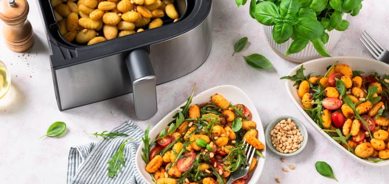 Gnocchi mit Ruccola und Tomaten auf weißen Tellern, daneben der Airfryer mit Gnocchi in der Schublade