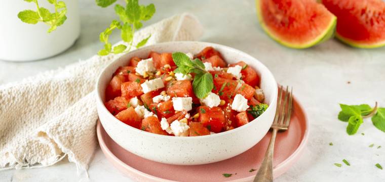 Wassermelone und Feta Salat in einer hellen Schüssel, daneben ein Tuch und Melone
