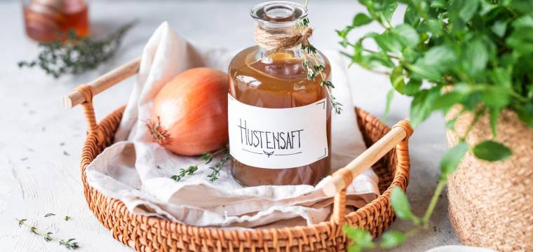 Eine Flasche Hustensaft und eine Zwiebel, daneben Kräuter Eine Flasche Hustensaft und eine Zwiebel, daneben Kräuter