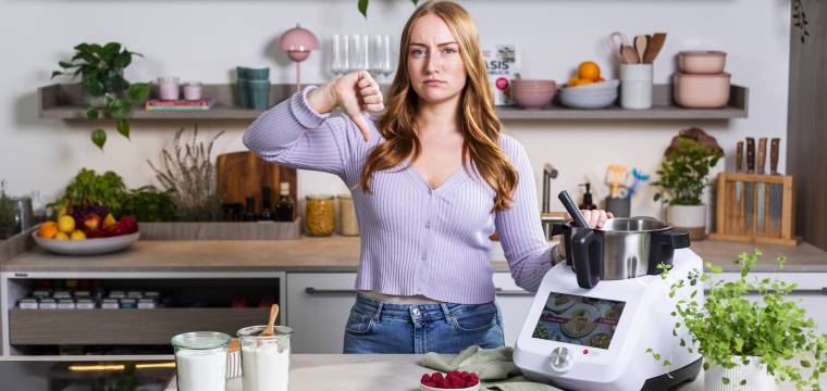 Frau steht in einer Küche neben dem Monsieur Cuisine und hält den Daumen runter Frau steht in einer Küche neben dem Monsieur Cuisine und hält den Daumen runter