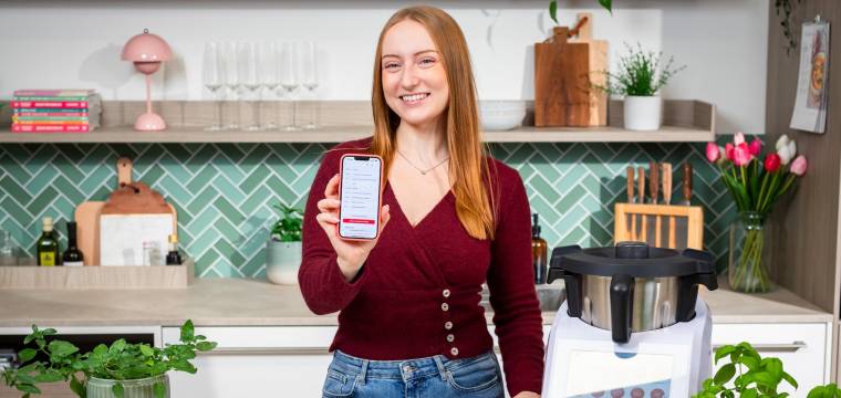 Isy von ZauberMix mit ihrem Telefon und dem Warenkorb von REWE auf dem Bildschirm