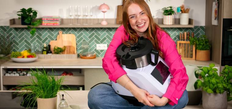 Eine Frau sitzt auf der Arbeitsplatte ihrer Küche und hält den Monsieur Cuisine im Arm
