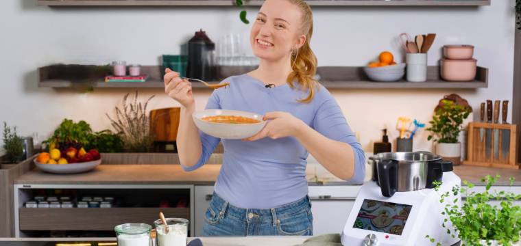 Junge Frau mit einem Teller Suppe neben dem Monsieur Cuisine Junge Frau mit einem Teller Suppe neben dem Monsieur Cuisine