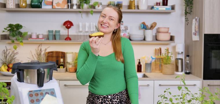 Junge Frau in einer Küche mit Monsieur Cuisine, hält eine Scheibe Brot in der Hand und freut sich